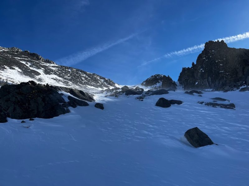 Foreground: Wind-packed surface snow. Background: blowing snow blasting facets off ridges and peaks.